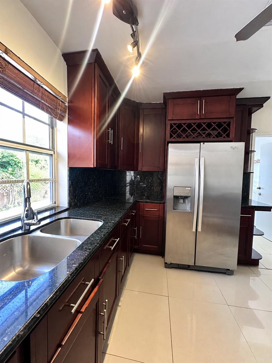 Kitchen featuring dark wood-finish cabinetry, stone countertops, integrated wine rack, stainless steel double-basin sink, and ceramic tile flooring