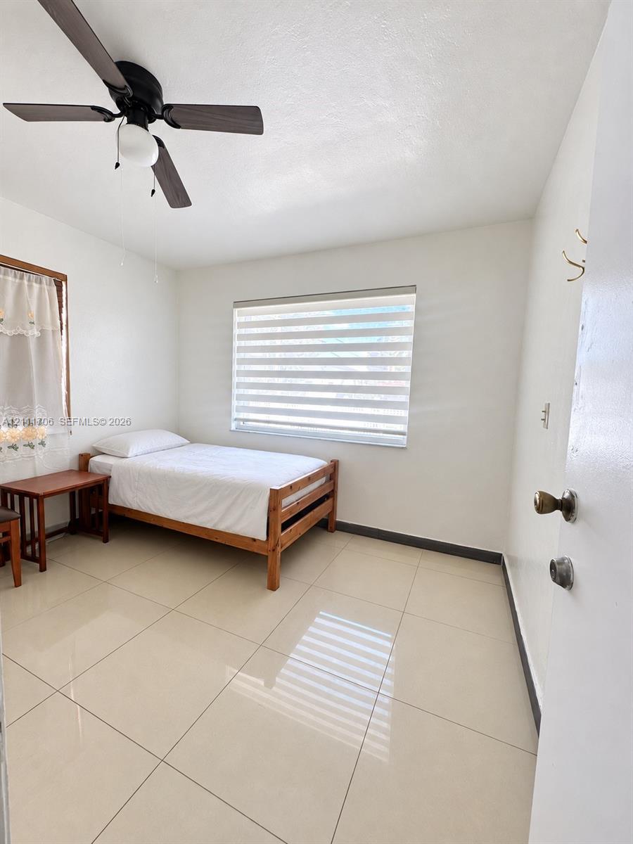 Large-format tile flooring, ceiling fan with integrated lighting, dual-layer window treatments, and white walls