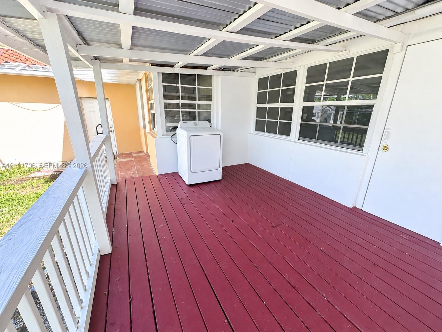 Covered porch featuring wood decking, white balustrades, a metal roof structure, and multi-pane windows