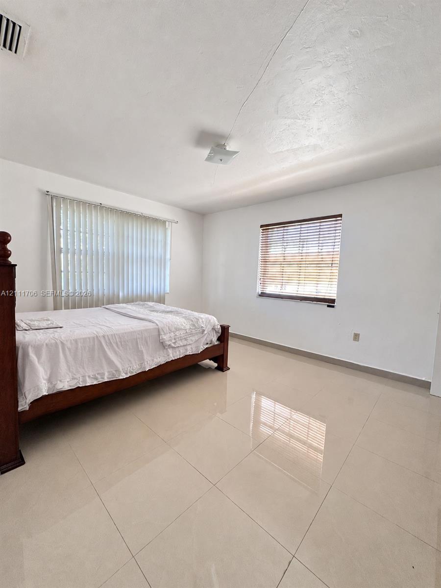 Spacious room with polished tile flooring, neutral wall finishes, vertical blinds, and horizontal slatted window treatments