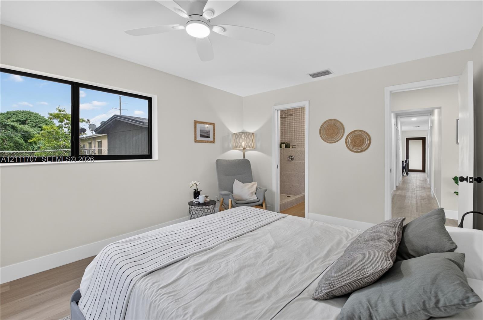 Neutral-toned interior featuring wood-finish flooring, a contemporary ceiling fan with integrated lighting, and large, black-framed picture windows