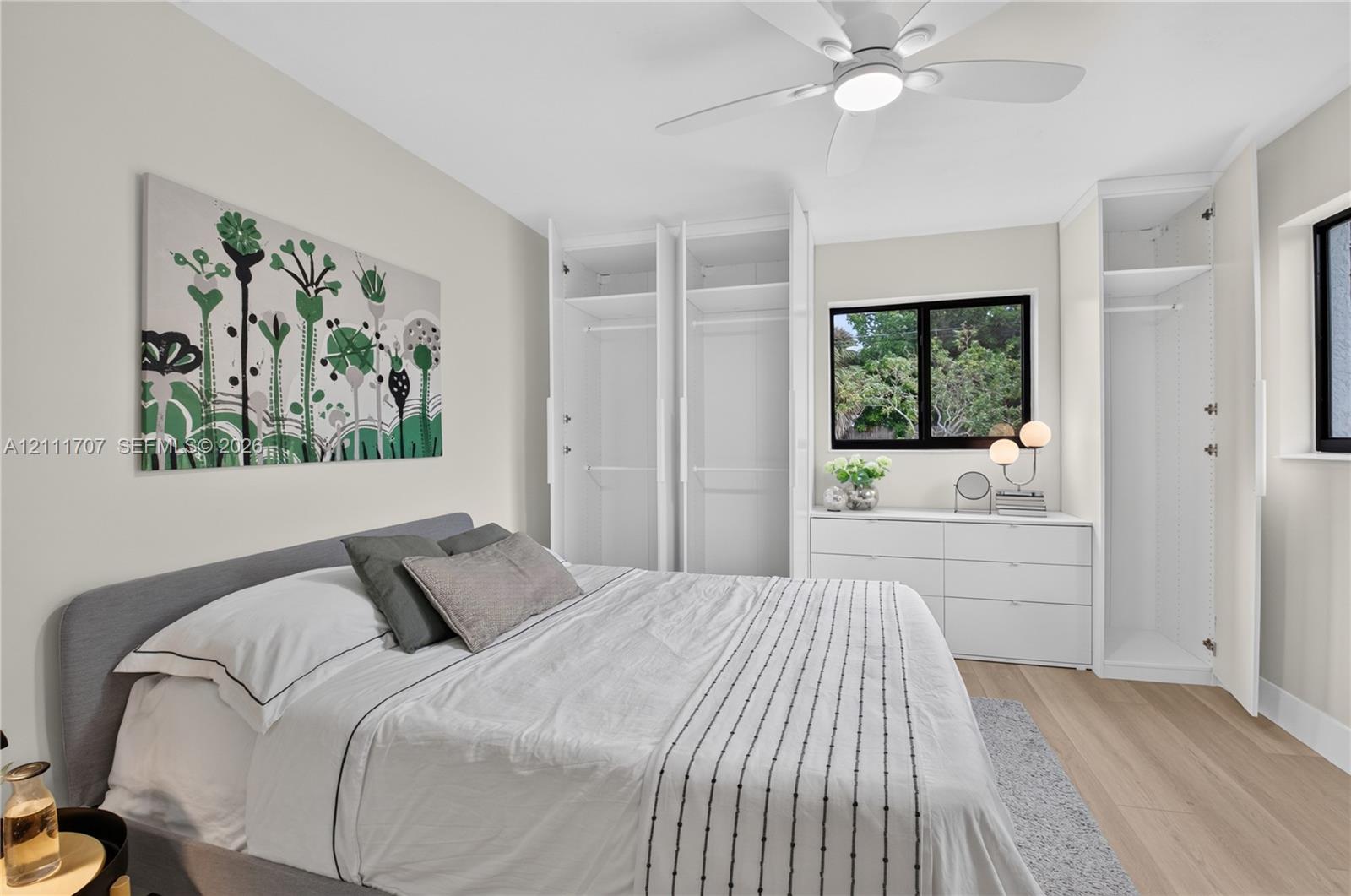 Built-in floor-to-ceiling closet cabinetry, light-toned wood-finish flooring, dual-pane windows with dark frames, and a modern ceiling fan with integrated lighting