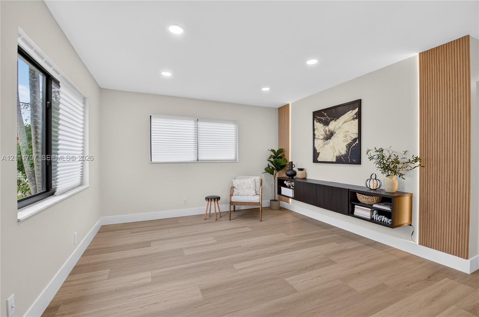 Living area featuring light wood-finish flooring, recessed lighting, horizontal slider windows, a wall-mounted floating cabinet, and vertical wood-slat accent panels with integrated lighting