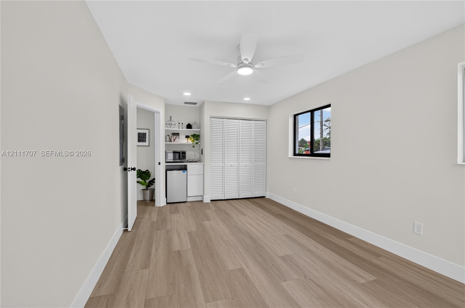 Interior space featuring wood-finish flooring, a ceiling fan with integrated lighting, recessed lighting, white louvered closet doors, and a built-in bar with cabinetry and open shelving