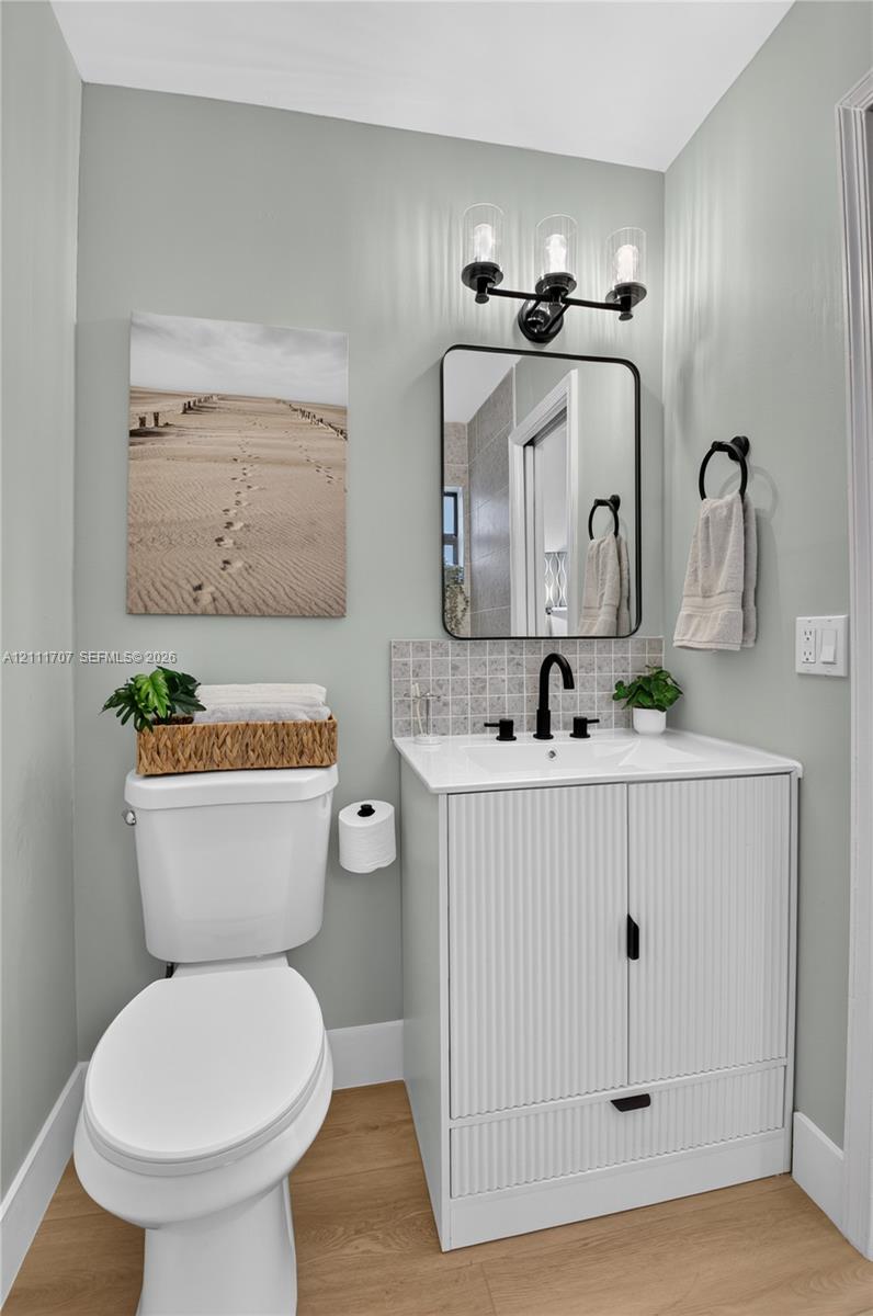 Modern vanity featuring a fluted cabinet design, rectangular white countertop, and matte black hardware, accompanied by a three-light fixture, framed mirror, and wood-finish flooring