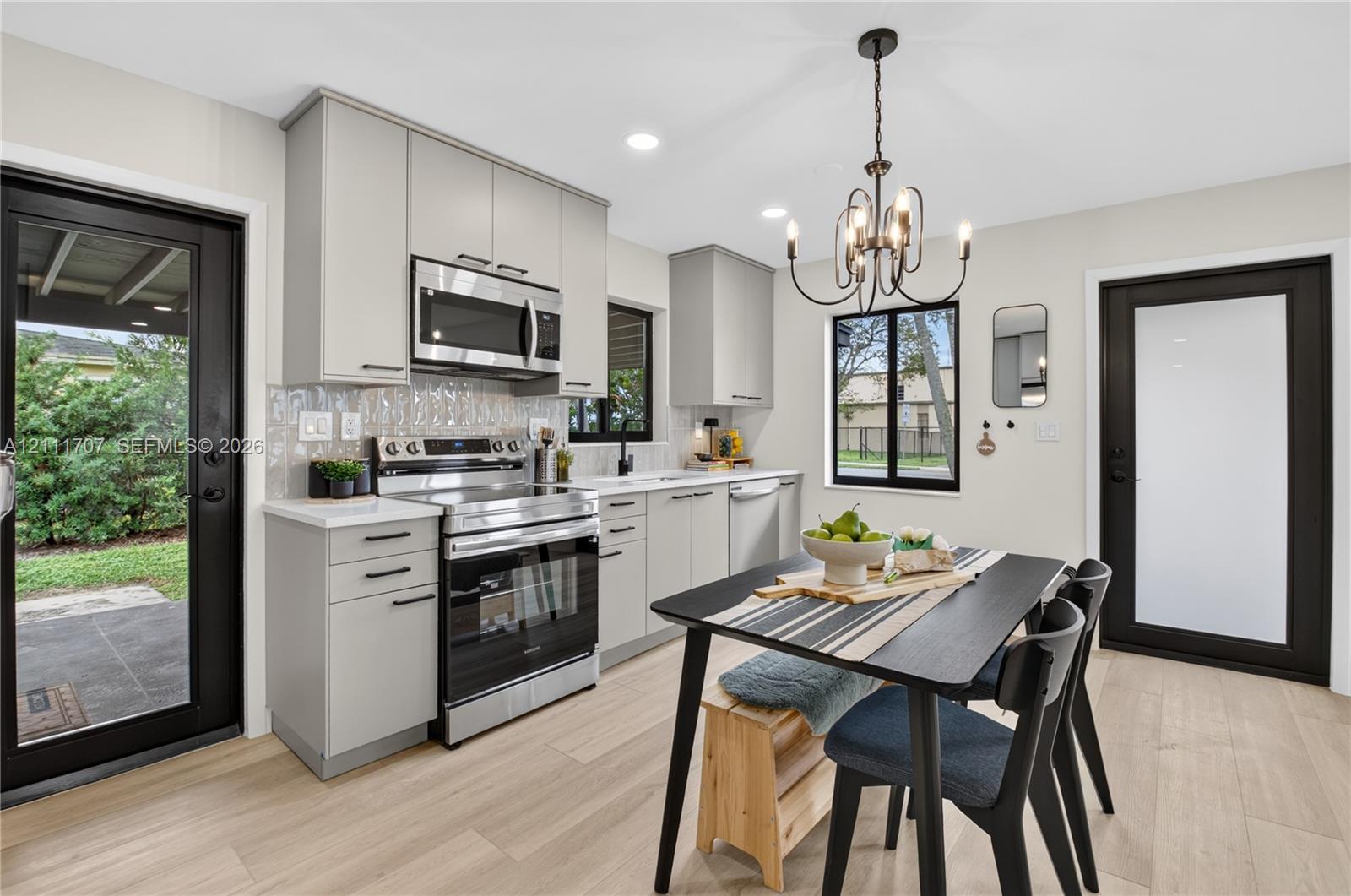 Kitchen featuring beige flat-panel cabinetry, stainless steel appliances, a textured tile backsplash, wood-finish flooring, and a multi-light chandelier