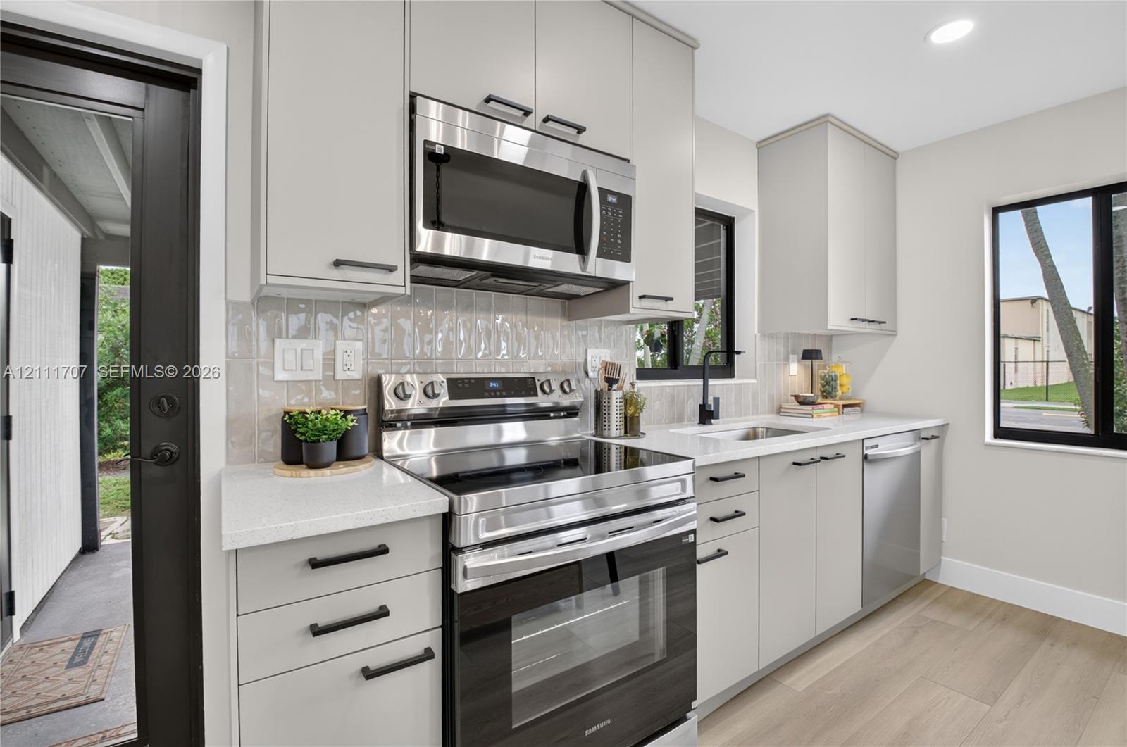 Kitchen featuring flat-panel beige cabinetry, stone-finish countertops, stainless steel appliances, a textured tile backsplash, and wood-finish flooring