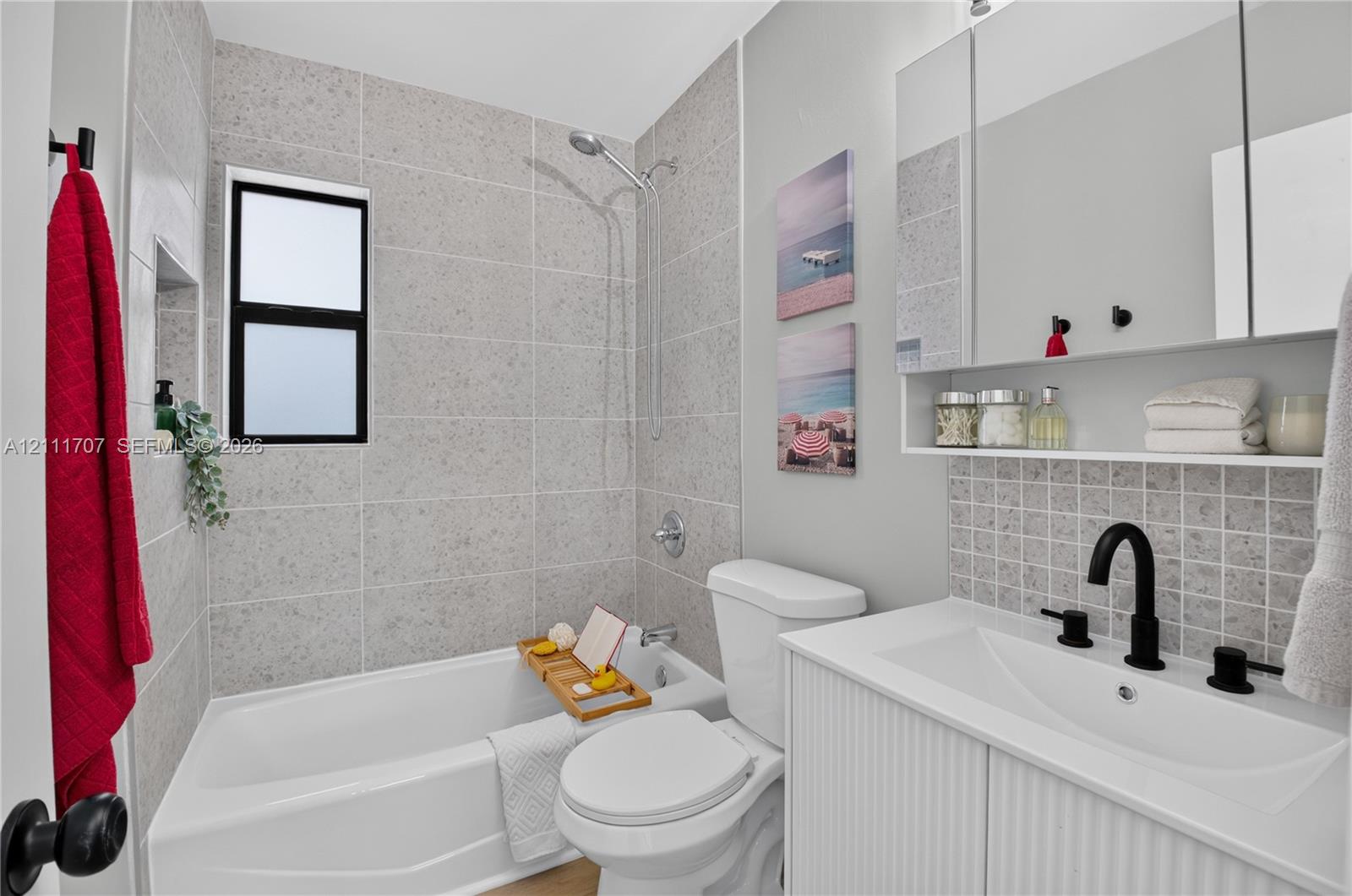 Bathroom featuring a white vanity with a rectangular sink, matte black fixtures, full-width mirrored medicine cabinet, a tiled shower surround with a built-in recessed niche, and a neutral-toned tile backsplash