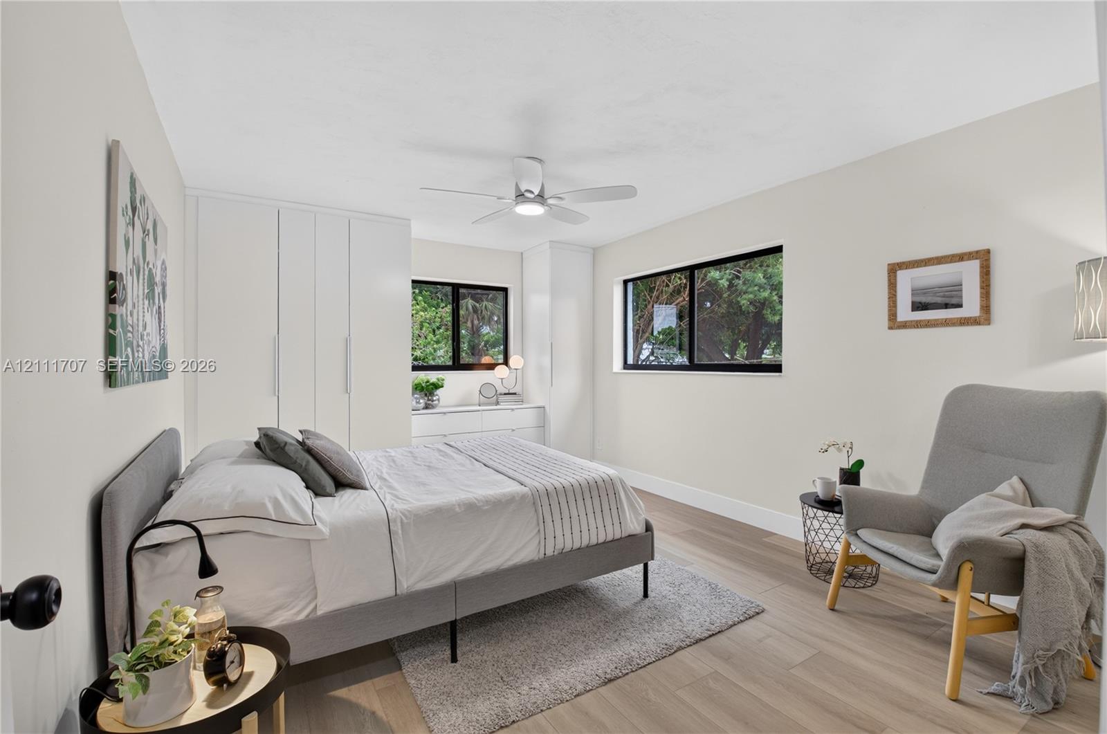 Bedroom featuring wood-finish flooring, floor-to-ceiling built-in closet cabinetry, dual black-frame windows, and a ceiling-mounted light fixture with integrated fan