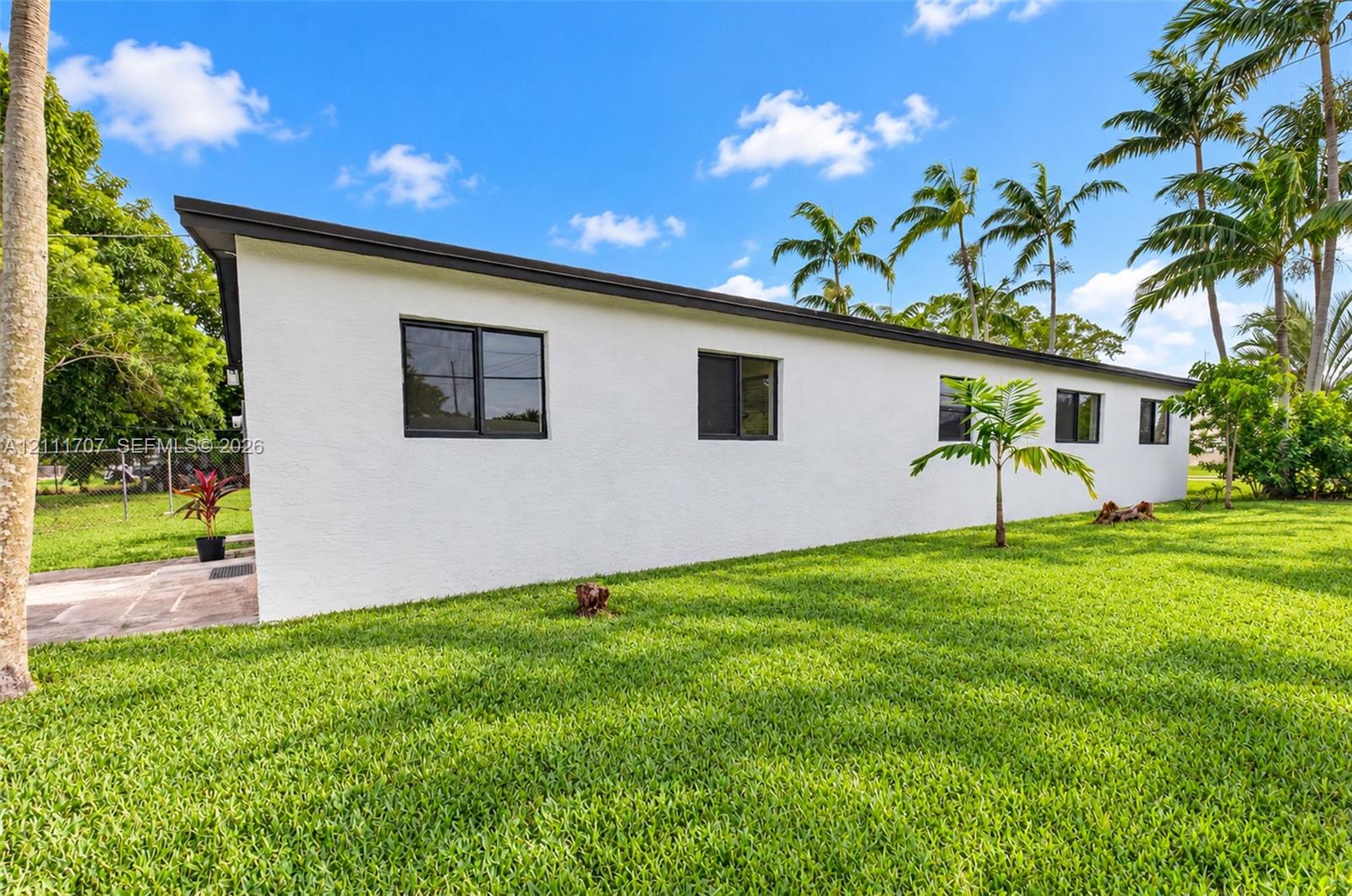 Exterior profile featuring white stucco siding, a flat roofline, dark-framed windows, and expansive green lawn