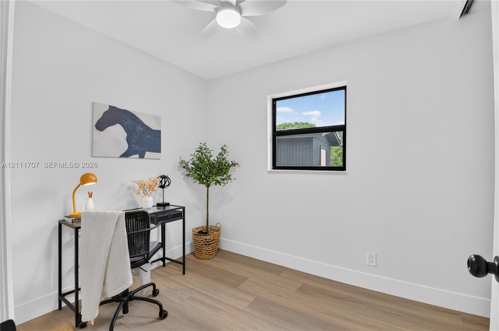 Room featuring wood-finish flooring, a matte black window frame, and a white ceiling fan with integrated lighting