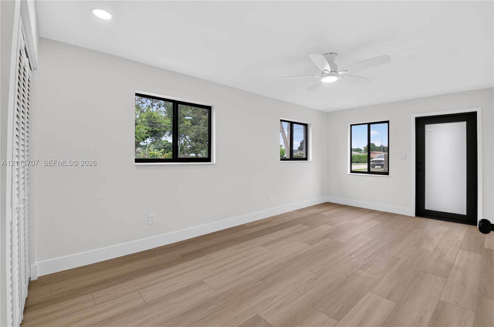 Light-filled room featuring wood-finish flooring, recessed lighting, a modern ceiling fan, multiple windows with black framing, and a frosted glass exterior door