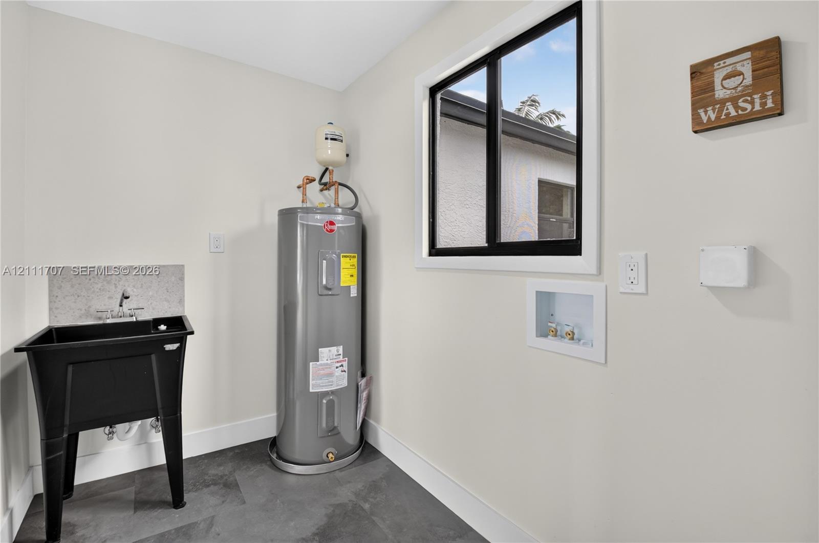 Utility area featuring slate-style flooring, a deep basin utility sink with a stone-finish backsplash, and a dedicated water heater
