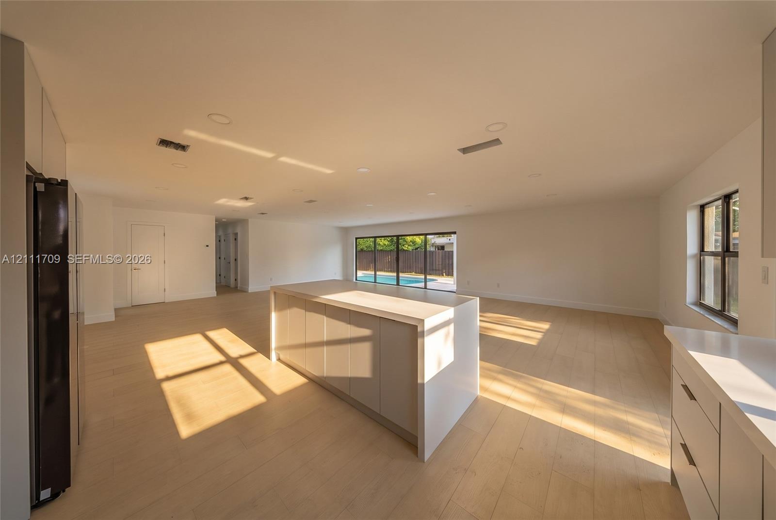 Open-concept interior featuring an oversized center island with stone-finish countertops, recessed lighting, wood-finish flooring, and multi-panel sliding glass doors