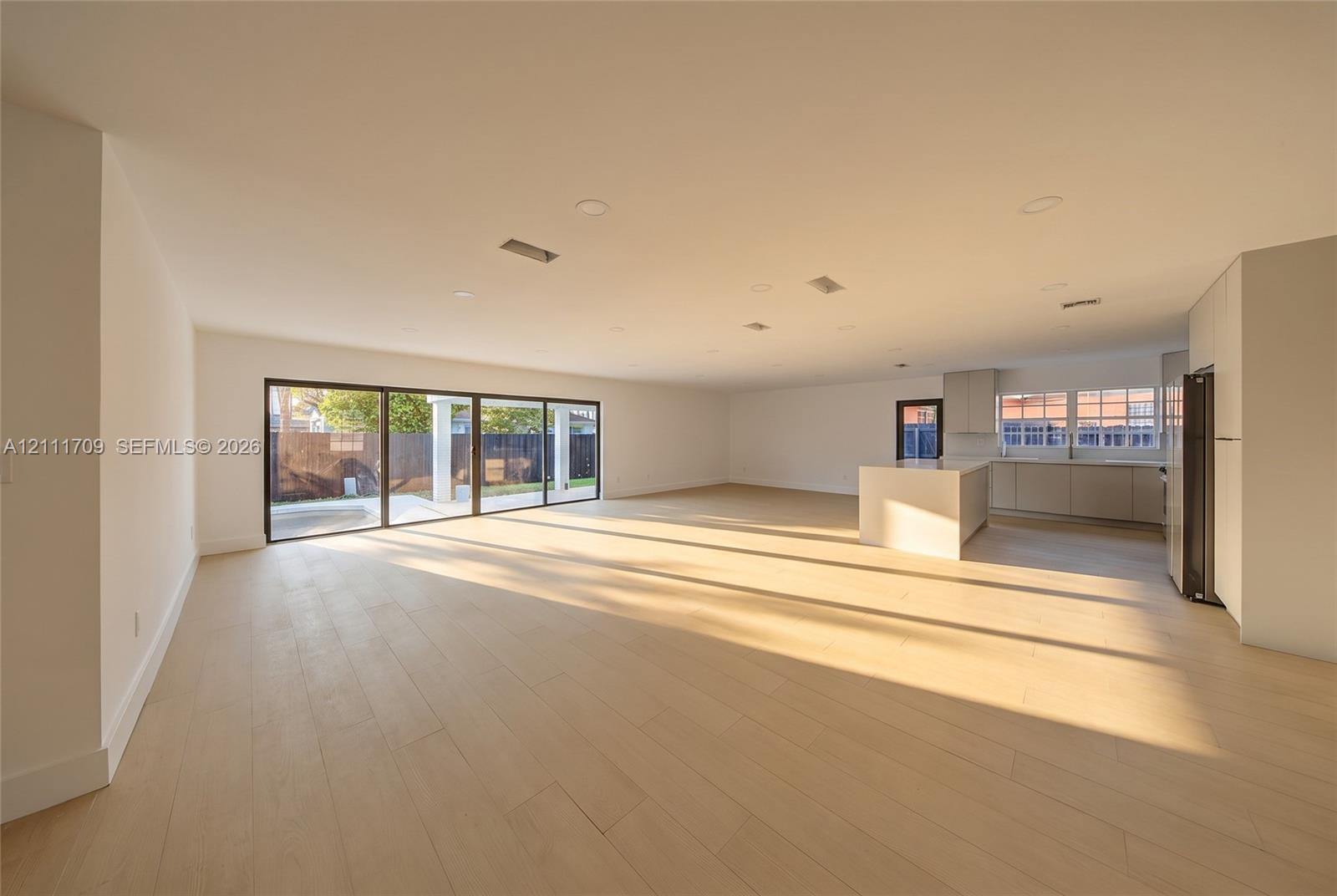 Open-concept floor plan featuring wood-finish flooring, recessed lighting, multi-panel sliding glass doors, and a central kitchen island with integrated cabinetry