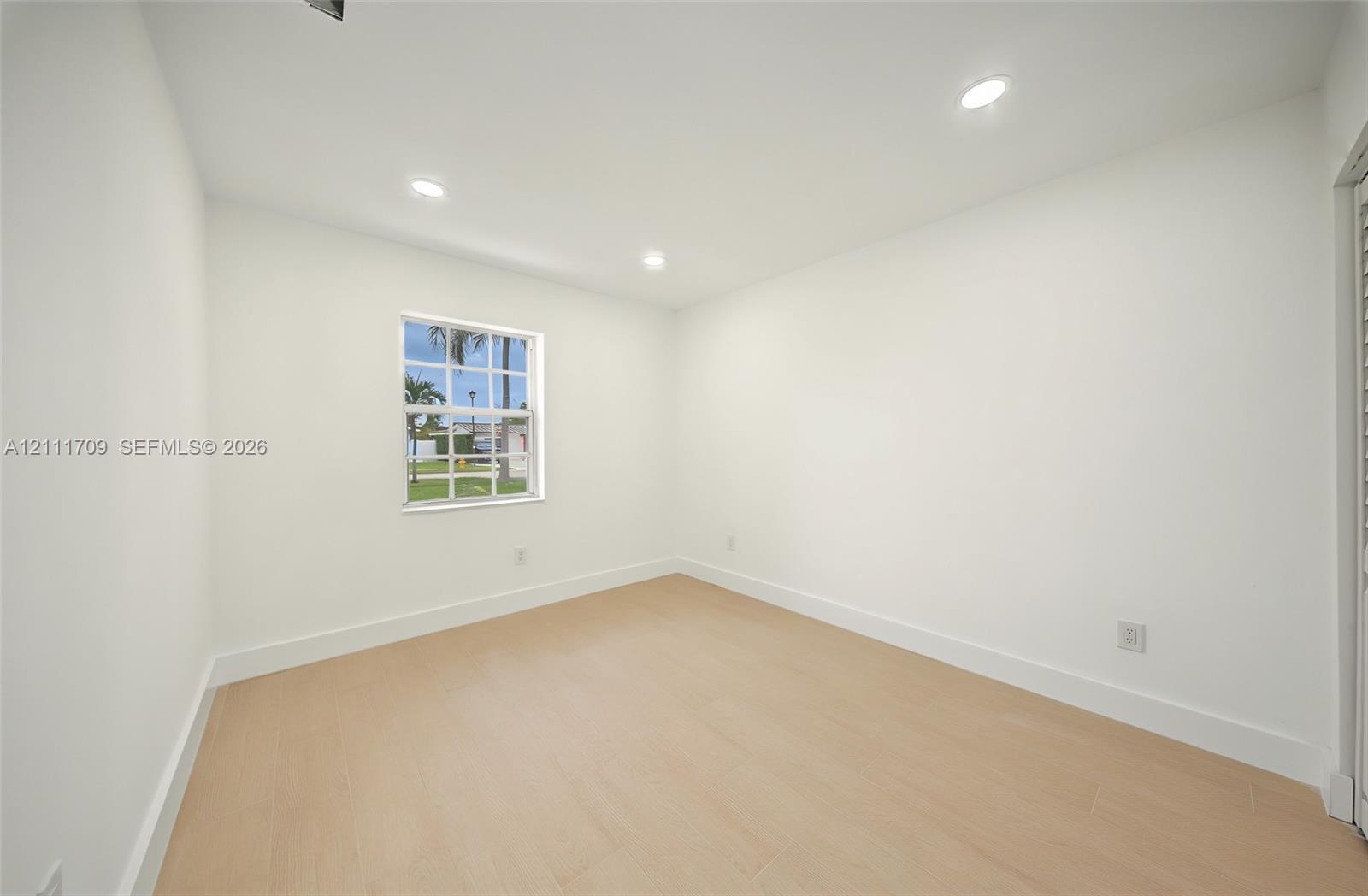 Neutral interior space featuring recessed ceiling lighting, light-toned wood-finish flooring, and a single-hung window with a muntin grid