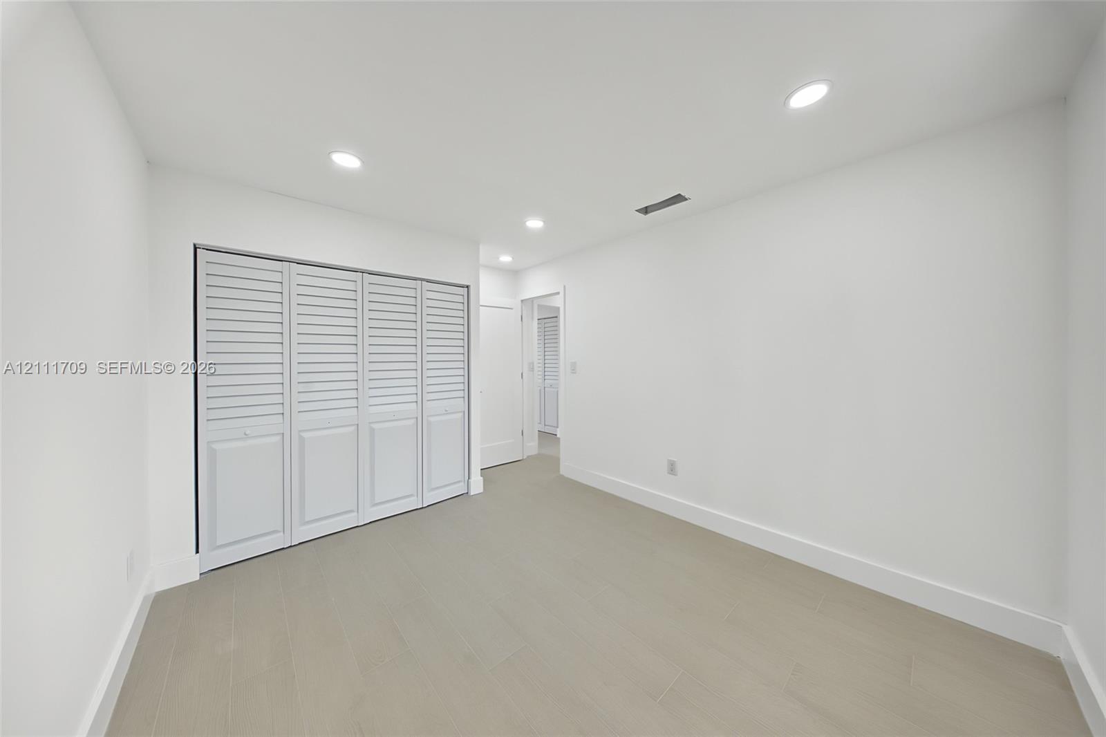 Neutral interior room featuring neutral-tone tile flooring, recessed ceiling lighting, and a multi-panel closet with louvered doors