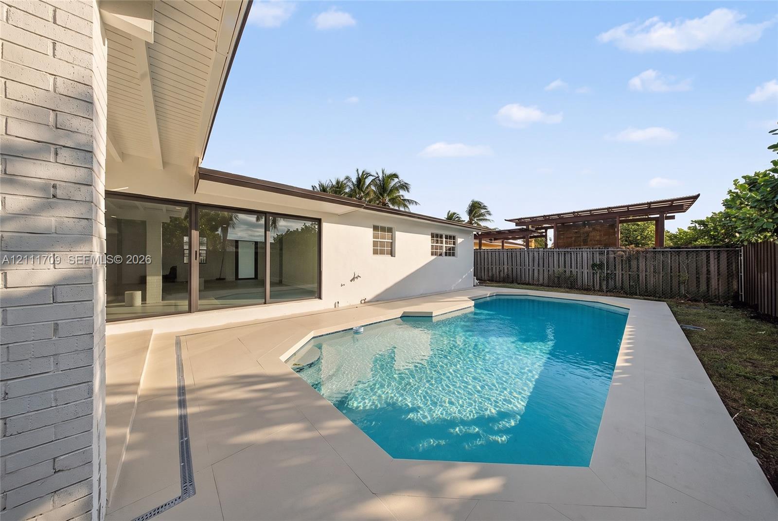 Backyard area featuring an in-ground swimming pool, expansive concrete patio decking, sliding glass exterior doors, and a wood-slat privacy fence