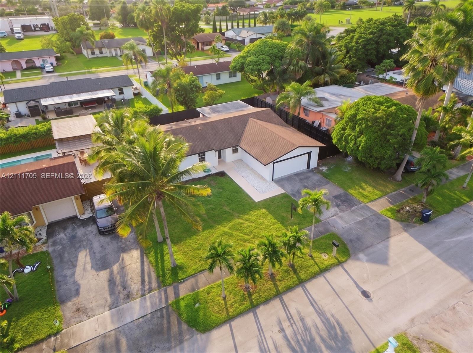 Single-story residence featuring a shingle roof, attached one-car garage, concrete driveway, and established palm landscaping
