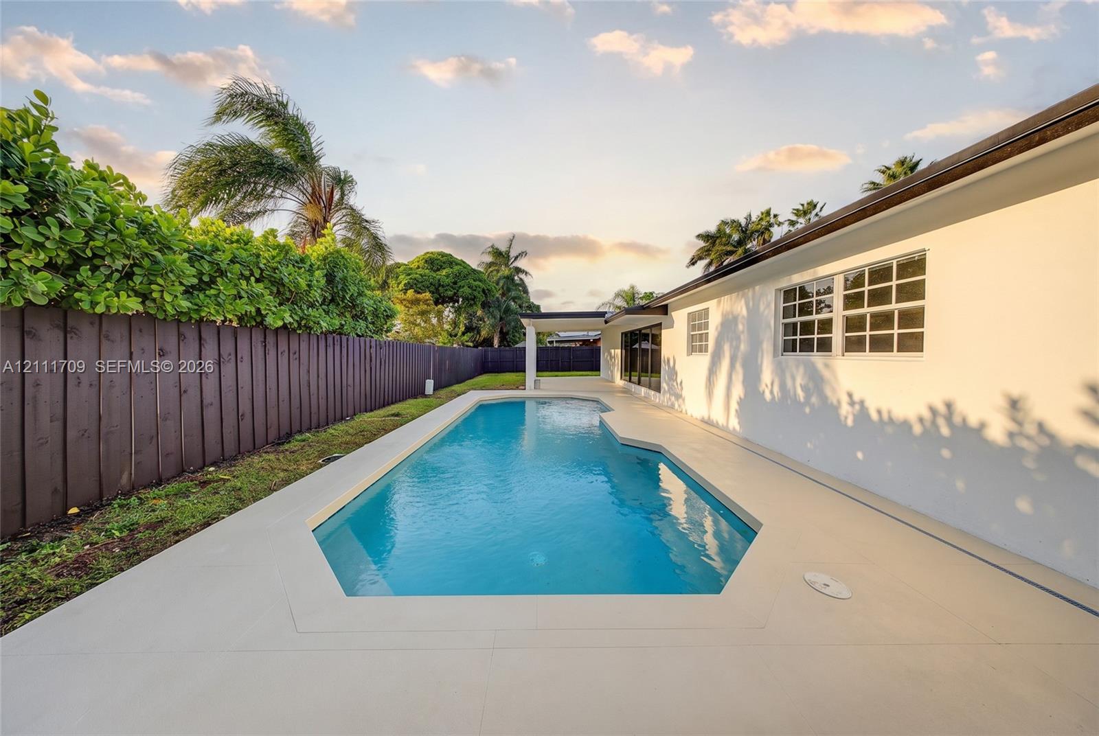 In-ground swimming pool with a concrete patio surround, covered outdoor area, and privacy fencing