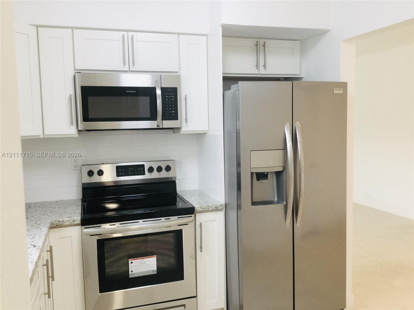 Kitchen featuring white shaker-style cabinetry, stone-finish countertops, stainless steel appliances, and an over-the-range microwave Kitchen featuring white shaker-style cabinetry, stone-finish countertops, stainless steel appliances, and an over-the-range microwave