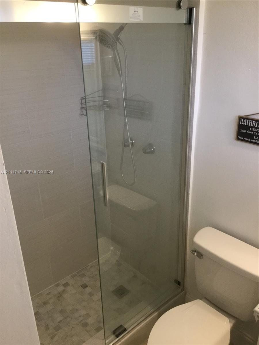 Walk-in shower enclosure featuring a sliding glass door, tiled walls, mosaic-tiled flooring, and a hand-held shower fixture