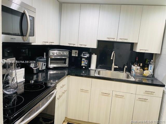 Kitchen featuring light-toned cabinetry with linear hardware, black solid-surface countertops, black backsplash, stainless steel sink with a goose-neck faucet, and stainless steel appliances Kitchen featuring light-toned cabinetry with linear hardware, black solid-surface countertops, black backsplash, stainless steel sink with a goose-neck faucet, and stainless steel appliances