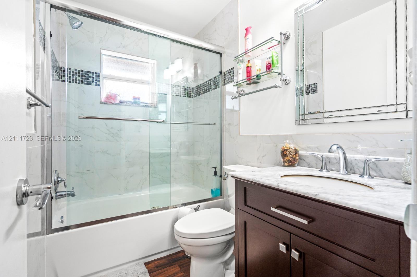 Bathroom featuring a dark wood-finish vanity with a stone countertop, an integrated undermount sink, a framed wall mirror, and a tiled tub shower combination with a glass sliding door