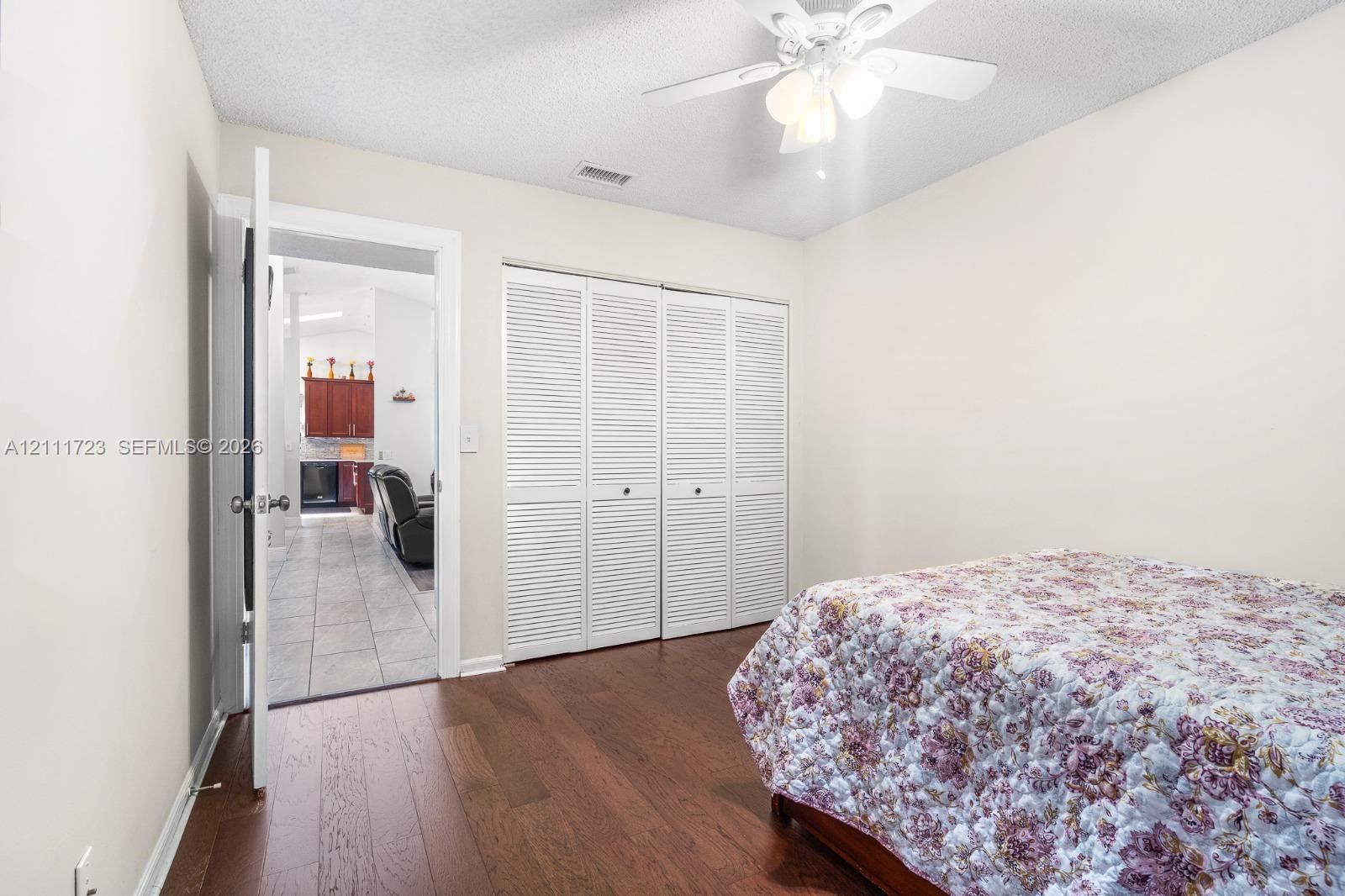 Interior room featuring wood-finish flooring, a ceiling fan with integrated light fixture, and double louvered closet doors