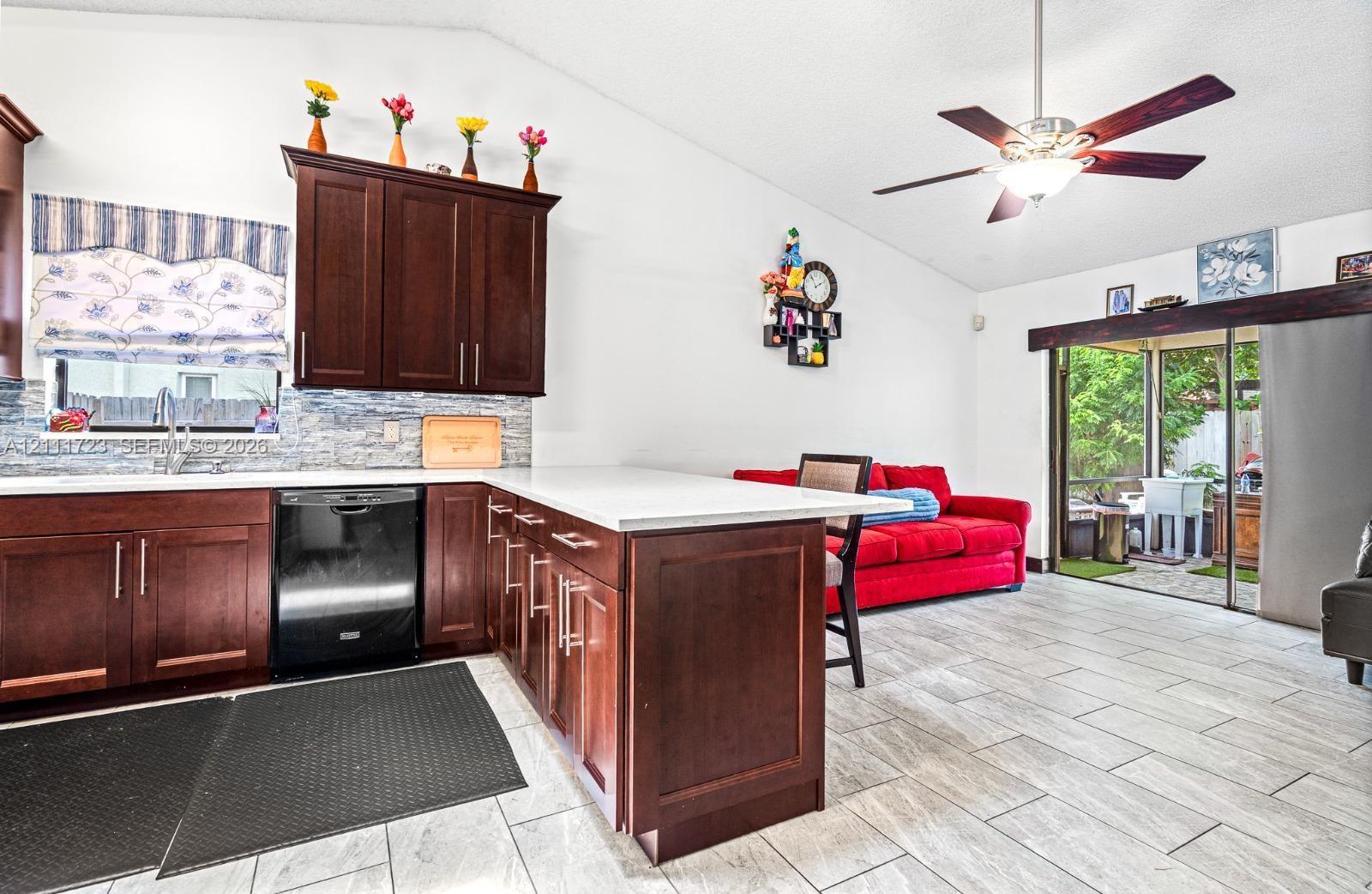 Kitchen featuring dark wood cabinetry, light-toned stone-finish countertops, tile backsplash, tile flooring, and a ceiling fan