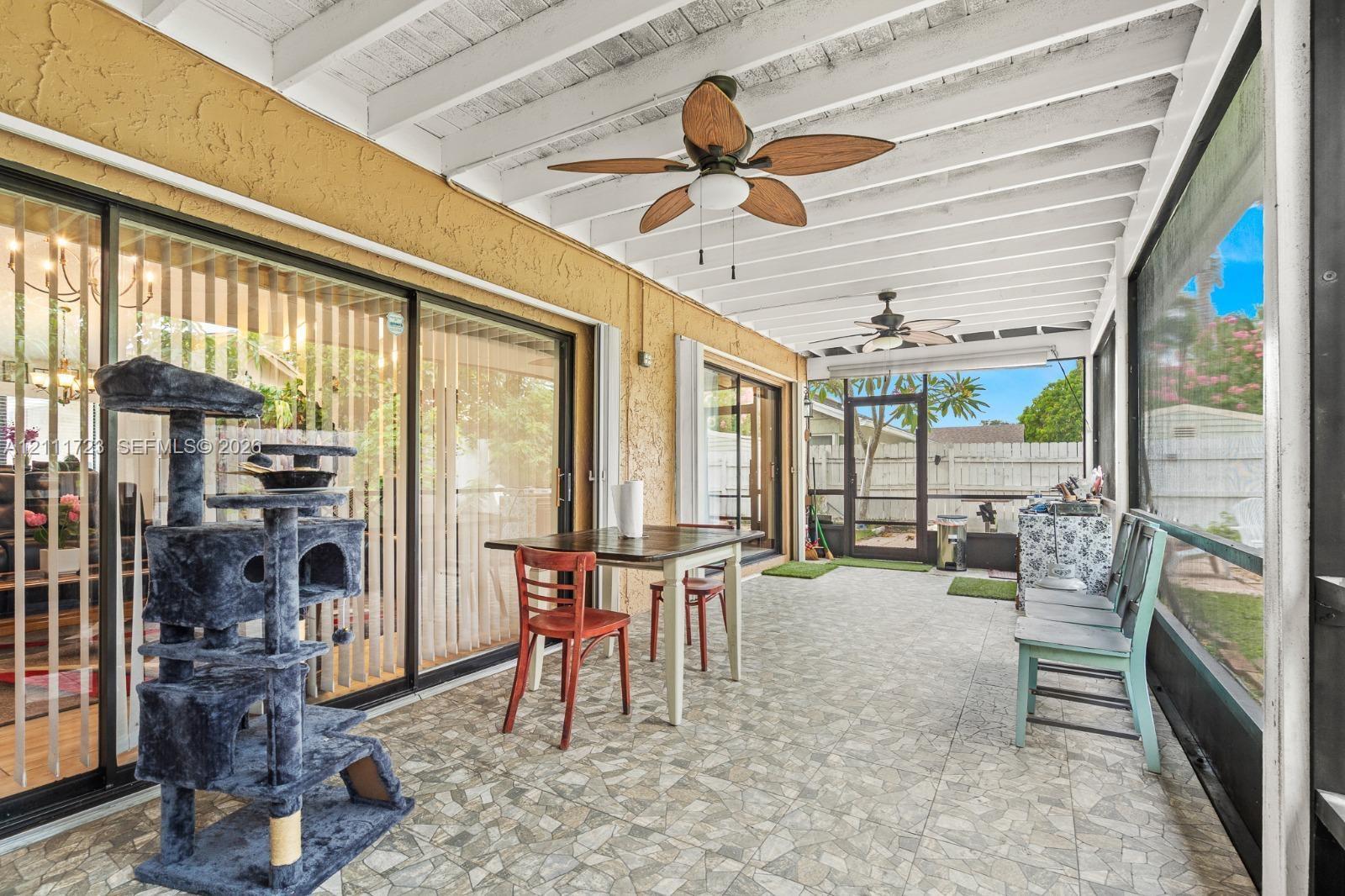 Screened-in patio featuring a textured concrete floor, white exposed-beam ceiling, and dual ceiling fans