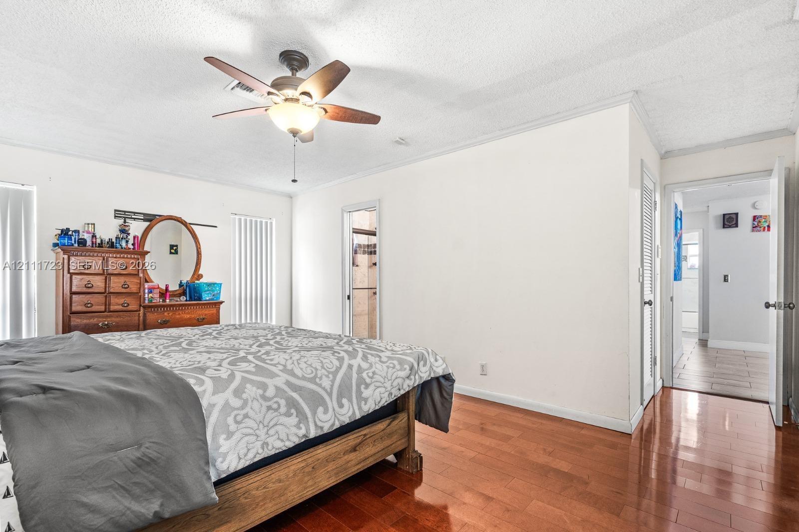 Room featuring wood-finish flooring, ceiling fan with integrated light fixture, crown molding, and vertical blinds
