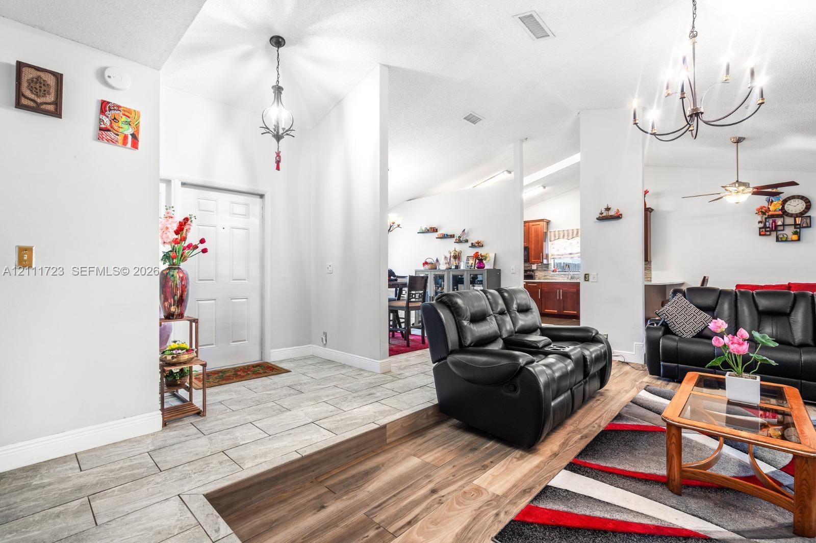 Open interior featuring vaulted ceilings, light-tone ceramic tile flooring, wood-finish flooring, and multi-arm chandelier lighting