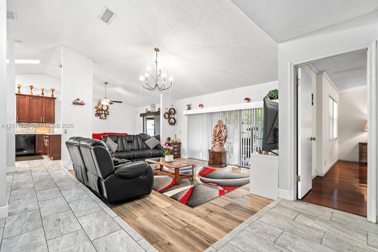 Open-concept living space featuring vaulted ceilings, wood-finish flooring, ceramic tile flooring, a multi-arm chandelier, and sliding glass doors
