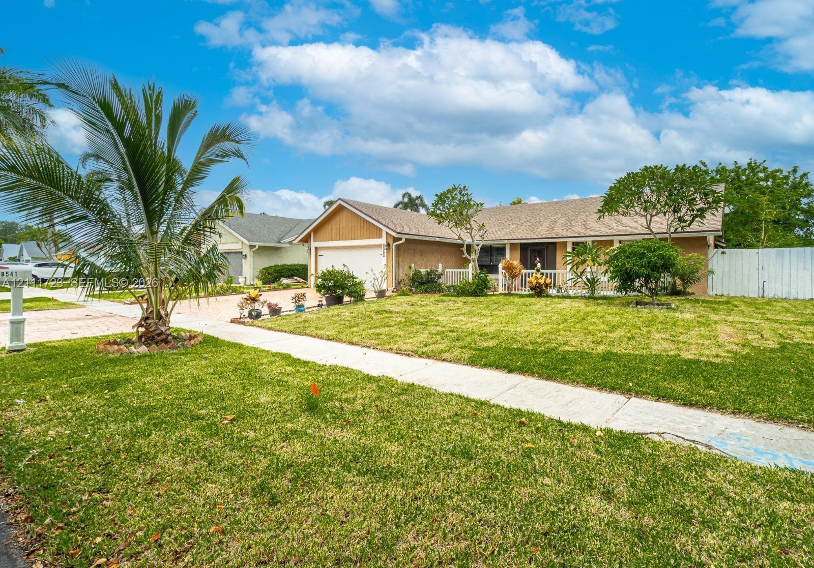 Single-story exterior featuring a shingled roof, attached two-car garage, covered entryway, and mature landscaping