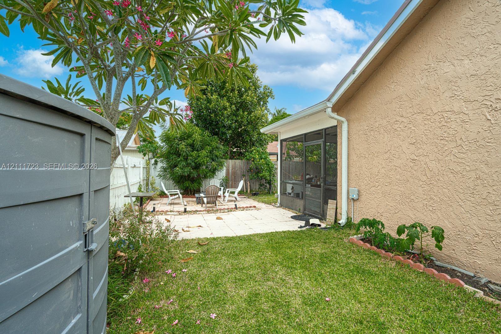 Rear exterior featuring a paved stone patio, screened-in enclosure, stucco siding, and a landscaped lawn with a raised garden border