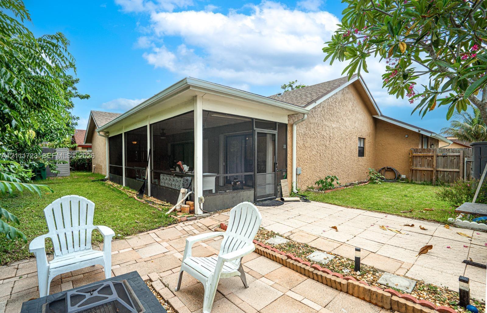 Rear exterior featuring a screened-in patio, concrete paver terrace, and grass lawn with a masonry border