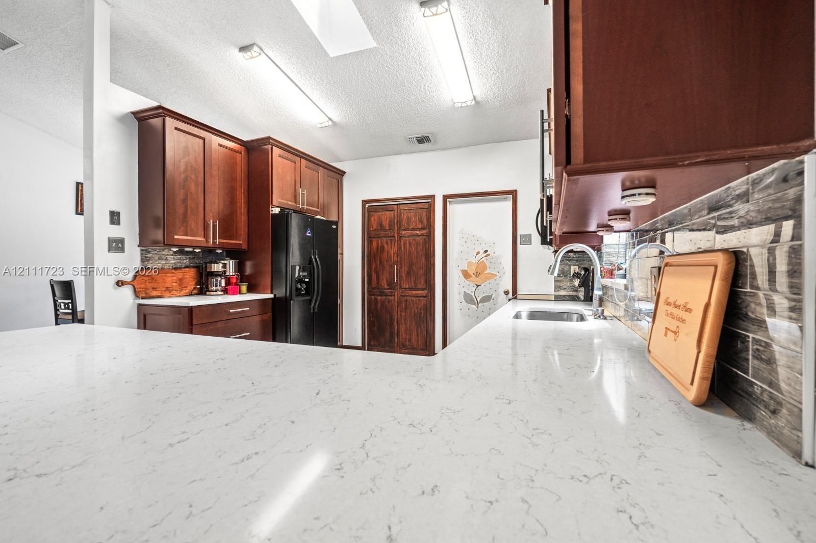Kitchen featuring stone-finish countertops, dark wood cabinetry, a stainless steel undermount sink with a gooseneck faucet, and a horizontally laid tile backsplash