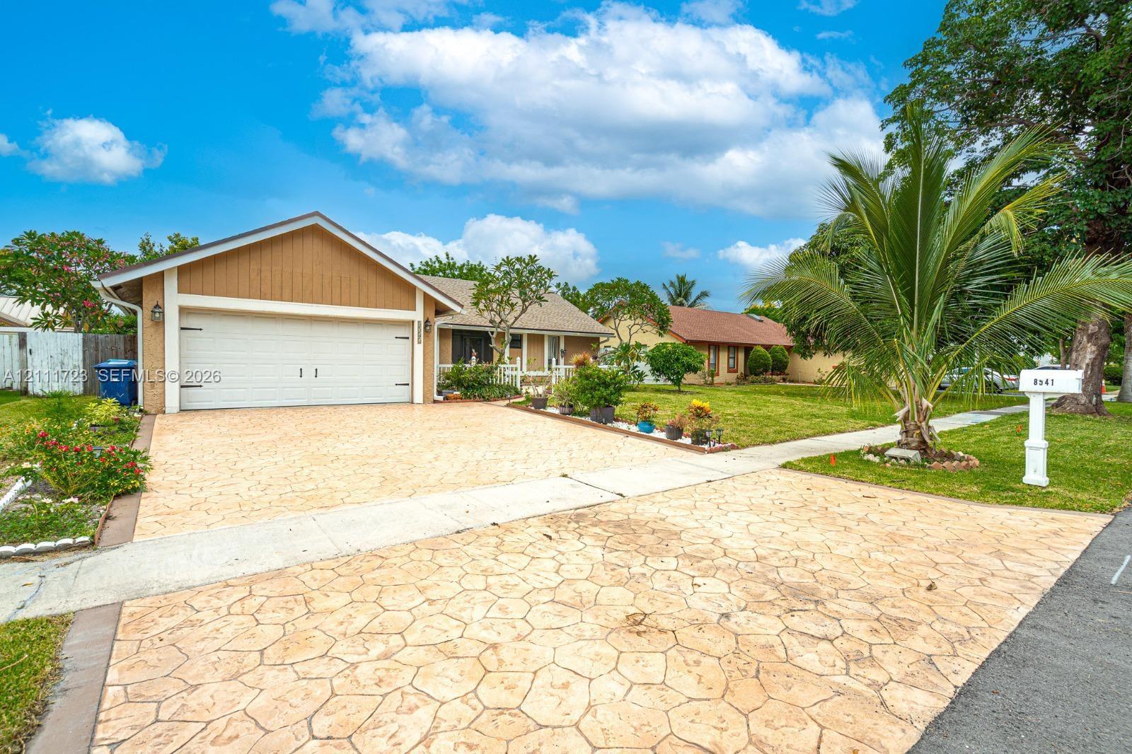 Single-story exterior featuring patterned concrete driveway, two-car garage, and mature landscaping