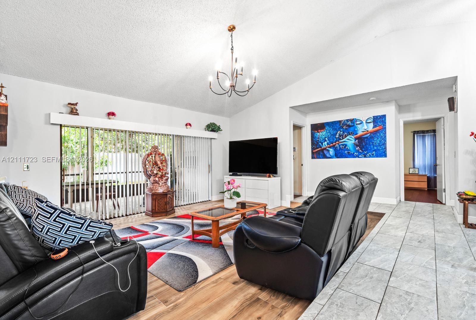 Living area featuring vaulted ceilings, wood-finish flooring, large sliding glass doors, and a multi-arm chandelier
