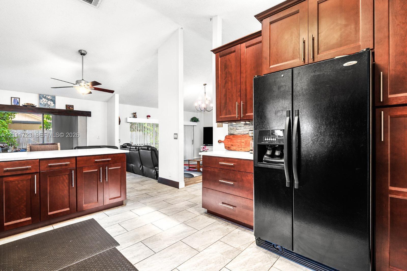 Kitchen featuring rich-toned wood cabinetry, stone-style countertops, large-format tile flooring, and a ceiling fan