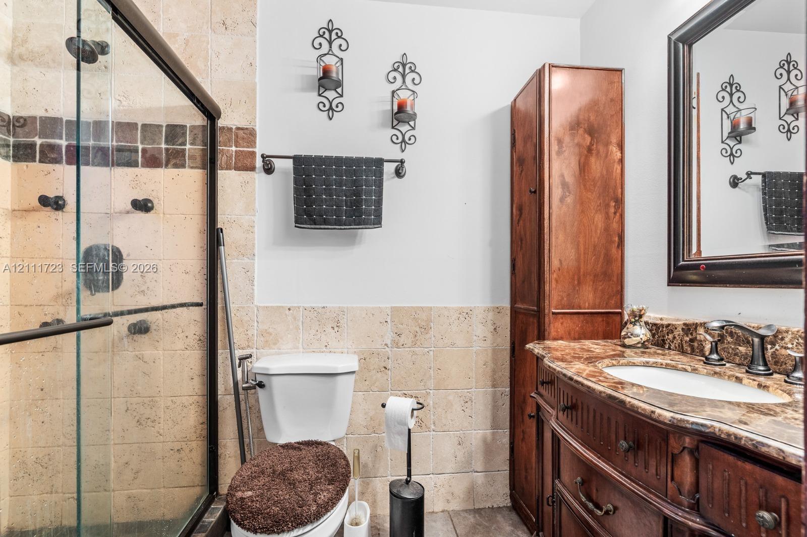 Bathroom featuring a glass-enclosed shower with tiled walls, built-in wooden cabinetry, stone-finish vanity countertop with an integrated basin, and a framed wall mirror