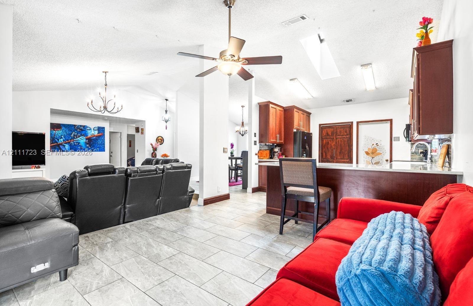 Open-concept interior featuring vaulted ceilings, tile flooring, kitchen cabinetry with a breakfast bar, skylights, and multiple ceiling fans