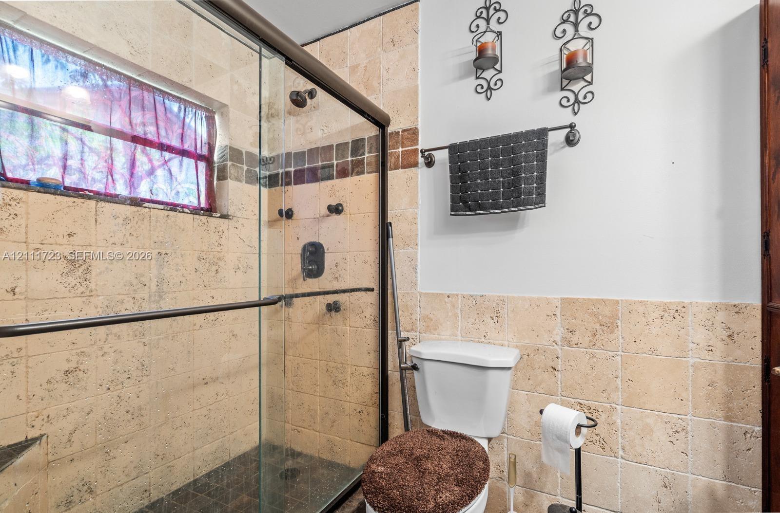 Walk-in shower featuring a frameless glass enclosure, natural stone wall tile with decorative mosaic inlay, and an integrated shower head