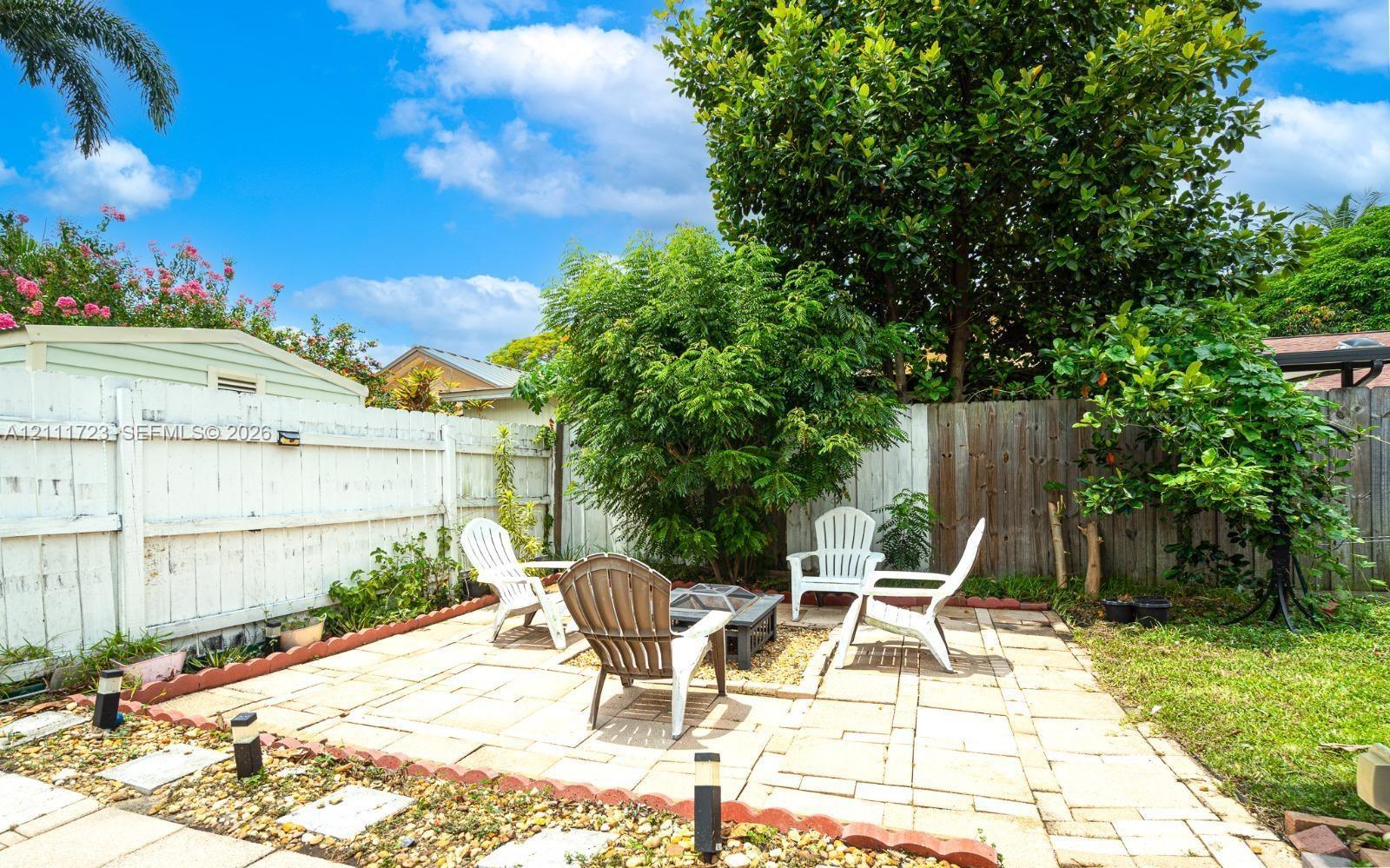 Backyard featuring a paved patio, perimeter wood fencing, mature trees, and garden edging