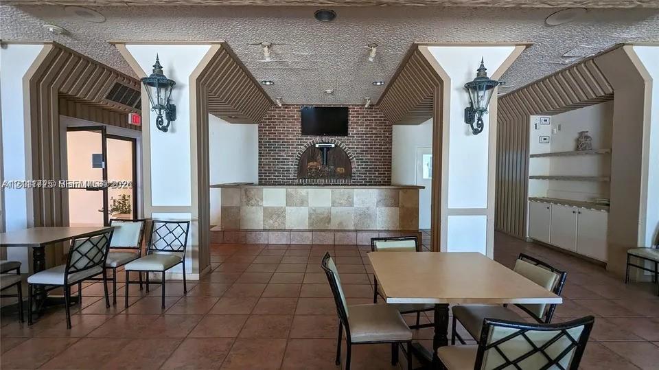 Built-in wet bar featuring a tile-faced counter, brick-accented wall, decorative columns, wall-mounted light fixtures, and integrated cabinetry