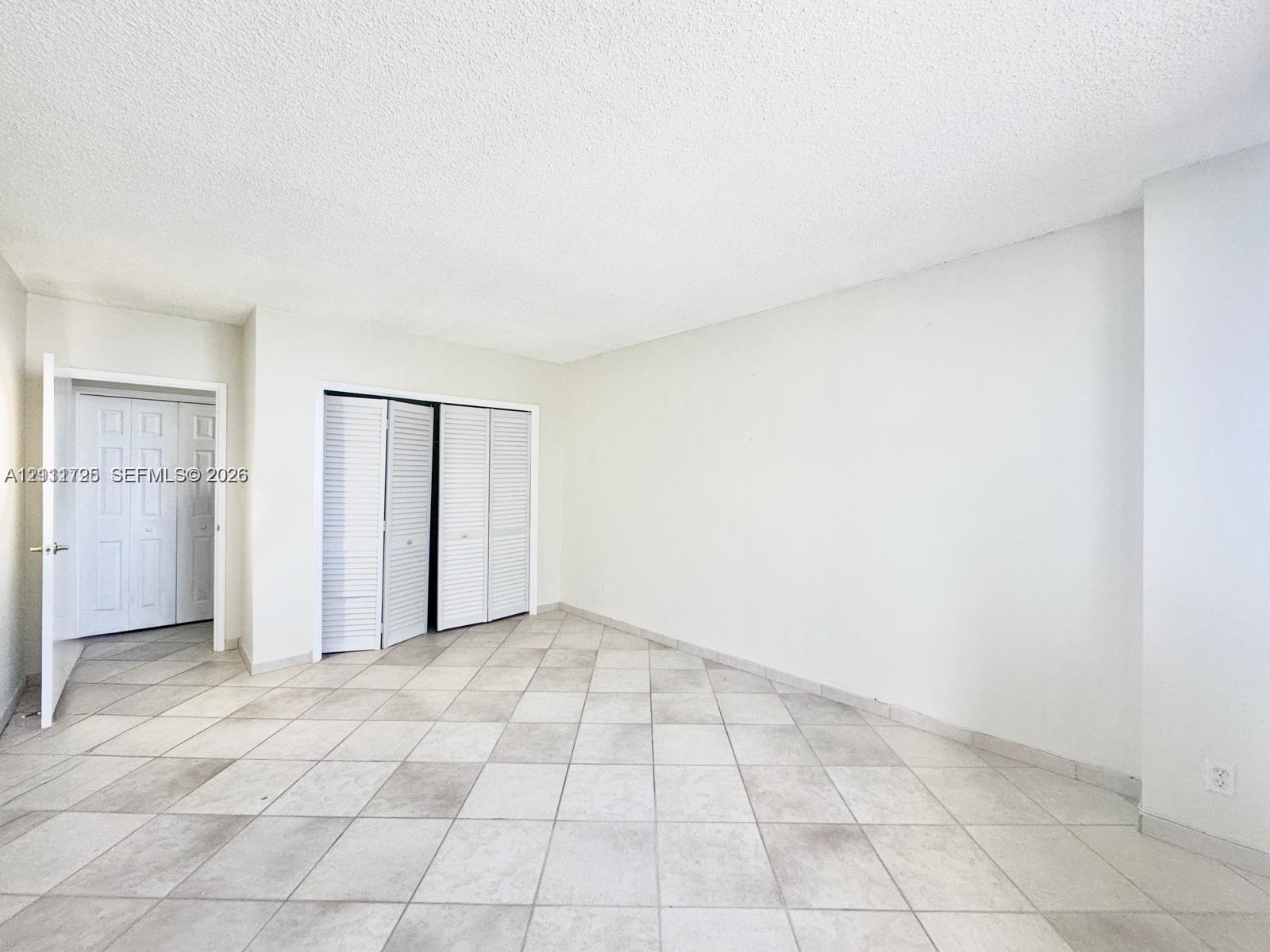 Neutral-toned tile flooring, white walls, and multiple sets of white louvered-door closets