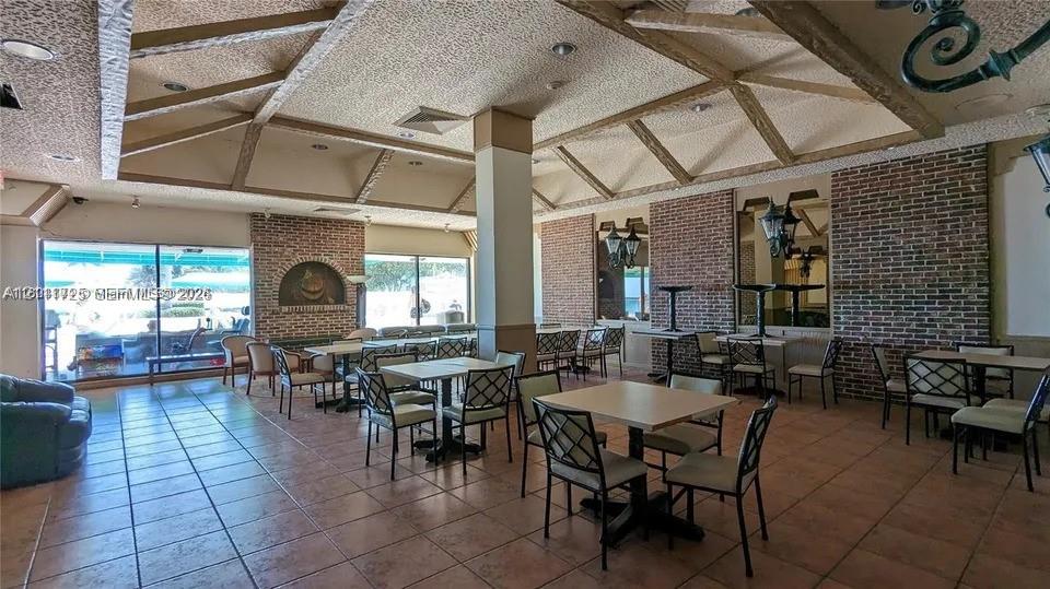 Vaulted ceiling with exposed wood beams, red brick accent walls, ceramic tile flooring, and large sliding glass doors