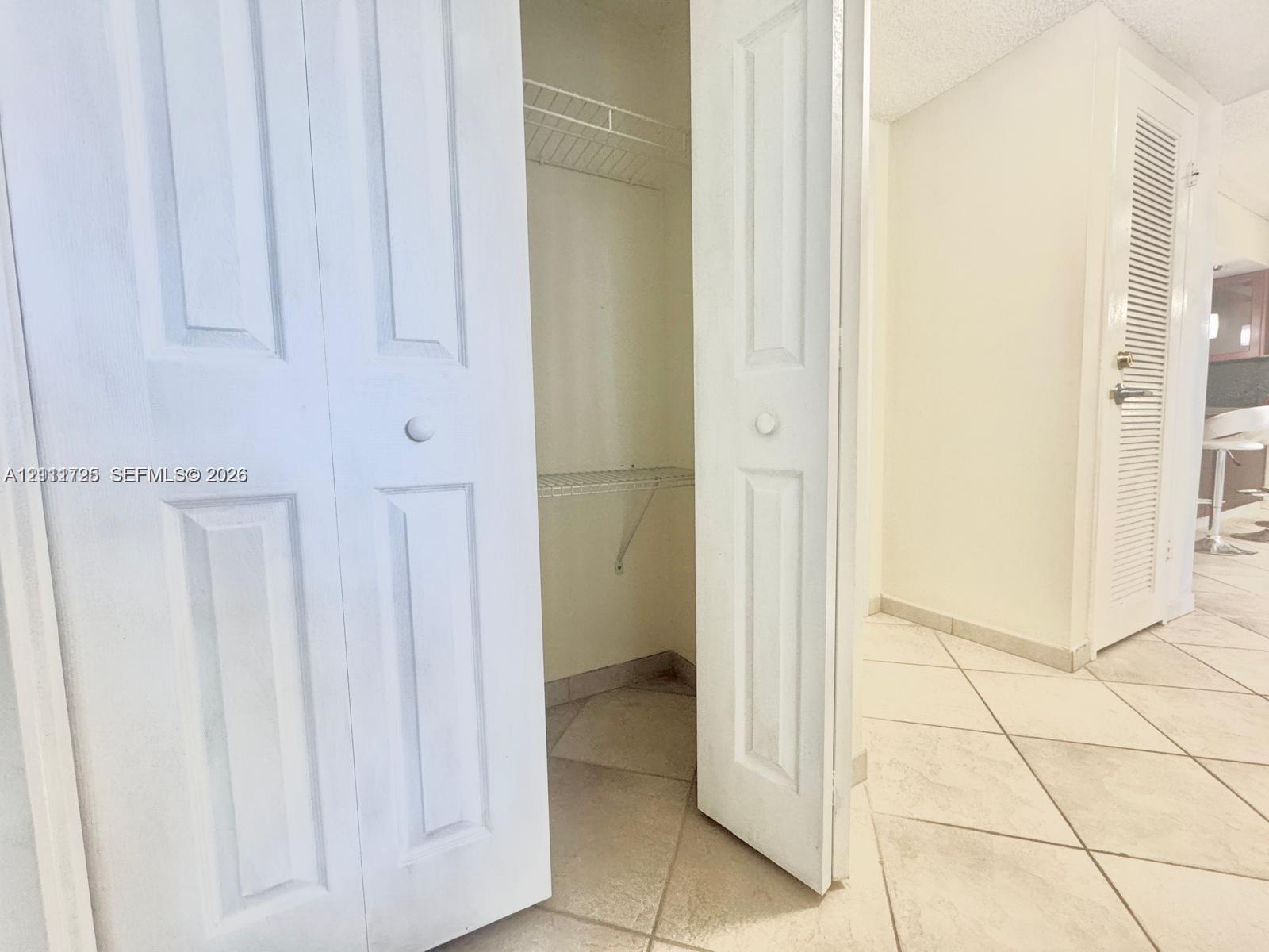 White bi-fold closet doors featuring panel detailing, integrated wire shelving, and neutral ceramic tile flooring