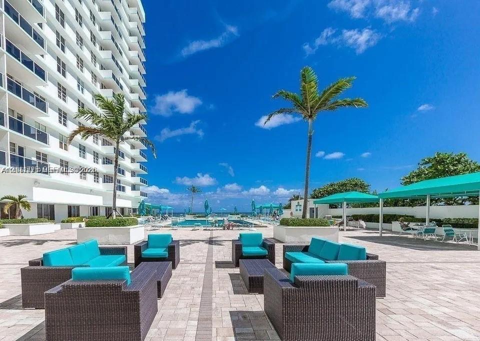 Paved pool deck featuring an in-ground swimming pool, decorative palm trees, built-in concrete planters, and shaded outdoor structures